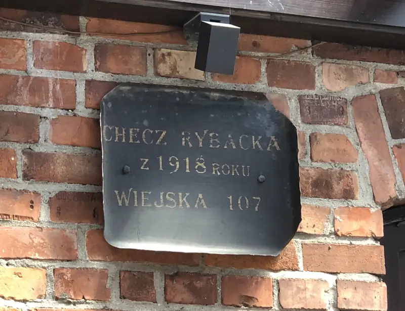 Metalowa tabliczka na ceglanej ścianie: Checz rybacka z 1918 roku, Wiejska 107